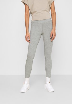 Leggings in cotone grigio con un design aderente, texture liscia e lunghezza alla caviglia, abbinati a sneakers bianche e un top beige.