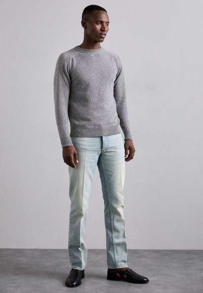 Maglione grigio a maglia con maniche raglan, jeans a gamba dritta blu chiaro e scarpe slip-on nere. Tessuto morbido e vestibilità casual.