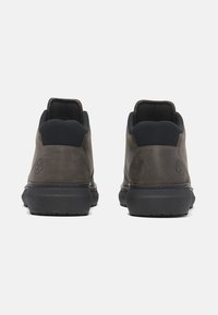 Sneakers in pelle marrone con accenti neri, design low-top, collare imbottito e suola in gomma. Presentano il logo sul tallone e una superficie testurizzata.