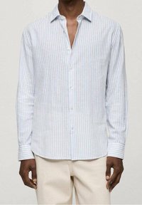 Jasnoniebieska, w paski, koszula z długim rękawem, wykonana z lekkiego materiału, z kołnierzykiem zapinanym na guziki i prostym dołem. Guziki są białe.