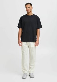 Sort oversized bomulds T-shirt med rund halsudskæring, parret med lyse, løstsiddende bukser og grå sneakers. Enkel, afslappet design.