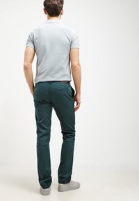 Herroutfit med en ljusgrå polo t-shirt och mörkgröna chinos. Chinosarna har en mjuk textur, knappstängning och bakfickor.