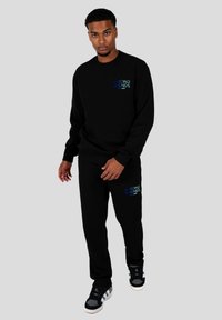 Conjunto de sudadera y pantalones de chándal negros, con "WRONG FRIENDS" en texto azul. La tela parece suave, con un ajuste relajado y un diseño minimalista.