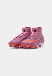 Lyserøde fodboldstøvler med høj ankeldesign, sorte detaljer og en livlig orange swoosh. Gennemsigtig sål med lilla og røde knopper.