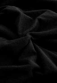 Tissu noir tordu au centre, montrant texture et plis dans un éclairage doux sur un fond sombre.