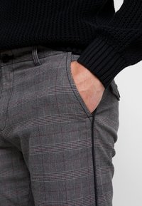 Grå rutiga byxor med röda accenter, med slim fit, fickor och en vävd textur, som är i kombination med en svart räfflad tröja.