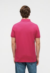 Πόλο με κοντά μανίκια, ζωηρό ροζ, με υφή υφάσματος. Διαθέτει κλασικό γιακά και άνετη εφαρμογή, συνδυασμένο με τζιν παντελόνια.