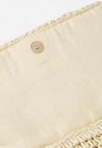 Sac en tissu beige avec des accents en paille tressée le long du bord, doté d'une fermeture à bouton pression doré près du sommet. Texture lisse.