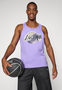 Débardeur violet arborant le logo des "Los Angeles Lakers" avec un graphique de basket-ball ; associé à un short en maille noir et tenant un ballon de basket.