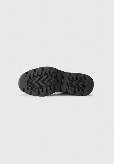 Semelle de chaussure en caoutchouc noir avec un motif texturé, comportant des rainures profondes et un design en zigzag pour une meilleure adhérence. Surface lisse avec des bords arrondis.