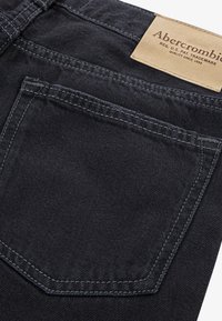 Crne traperice od denima s stražnjim džepom s kontrastnim šavovima, kožnom oznakom branda i mekanim, teksturiranim završetkom.