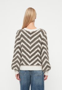 Šedý a biely sveter s chevron vzorom, s textured, fuzzy povrchom, rebrovanými manžetami a širokým okrúhlym výstrihom. Skombinovaný s modrými džínami.