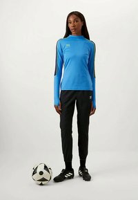Camisa deportiva de manga larga azul con cuello alto y pantalones de chándal negros, combinados con botas de fútbol negras y un balón de fútbol en blanco y negro.