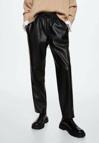 Czarne spodnie z ekoskóry o luźnym kroju, z elastycznym paskiem na sznurki, kieszeniami bocznymi i minimalistycznymi detalami szwów, zestawione z czarnymi botkami za kostkę.