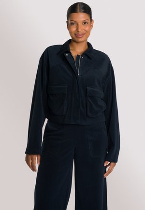 Marineblauwe corduroy jas met een kraag, ritssluiting en twee voorzakken; gecombineerd met bijpassende wijde broek met een gladde textuur.