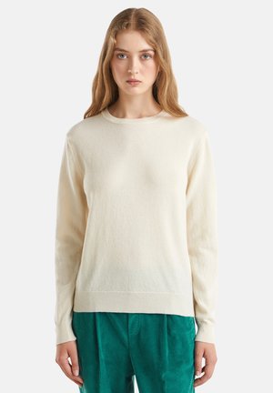 Roomkleurige trui met een ronde halslijn en lange mouwen, gemaakt van een zacht materiaal. Heeft ribgebreide manchetten en een zoom, gedragen met groene corduroy broek.