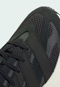 Čierna športová obuv s mesh zvrškom, semišovými a syntetickými prvkami, plochými šnúrkami a textúrovanou podrážkou pre lepšiu priľnavosť.