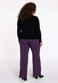 Zwarte lange mouwen top gecombineerd met paarse gepatternde broek met een grafisch ontwerp. De broek heeft een rechte pasvorm en een lichte uitloop bij de zoom.