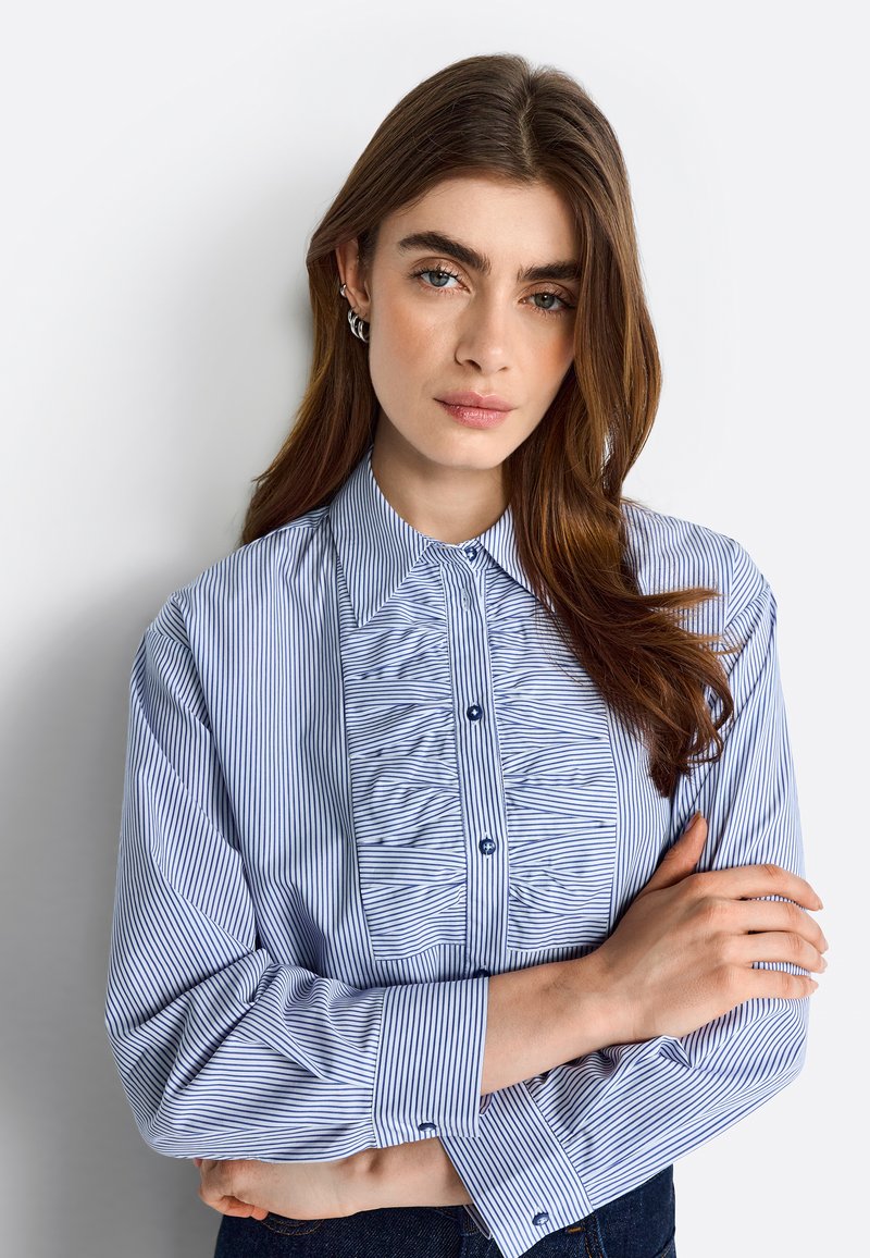 Blue and white striped blouse with a button-down collar, pleated front detail, and long sleeves. Made of lightweight fabric with subtle sheen.