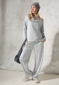Lichtgrijze sportoutfit met een ronde hals sweatshirt en wijde broekspijpen, gecombineerd met een grijze gebreide beanie en een donkergrijze schoudertas.