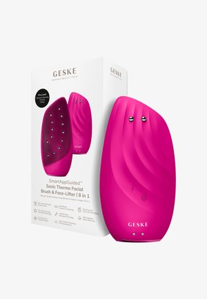 Felroze 8-in-1 sonische thermo gezichtsborstel en face-lifter apparaat met getextureerde en gladde zijkanten, naast witte verpakking.