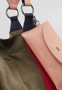 Grüne und rote Stofftasche mit Lederakzenten. Verfügt über eine rosa Lederbörse, die mit Metallringen befestigt ist; strukturierte Oberfläche, minimale Hardwaredetails.