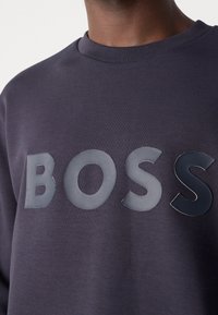 Navy sweatshirt med djärv, glansig "BOSS"-logotyp på framsidan. Tillverkad av mjukt, texturerat tyg med en klassisk crew neck-design.