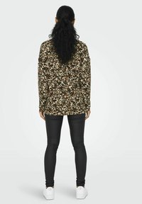 Langærmet top med et brunt og grønt blomsterdesign, parret med sorte leggings og hvide sneakers. Textureret stof og afslappet pasform.