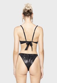 Zwart bikini set met dunne verstelbare bandjes, striksluiting op de rug en glanzende stofstructuur. Hoog uitgesneden slip met geraffineerde details aan de zijkanten.
