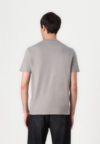 Camiseta gris de mangas cortas con cuello redondo, hecha de una tela suave, con un diseño minimalista y un dorso liso. Combinada con jeans oscuros.