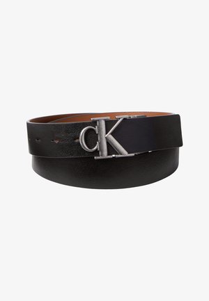 Cintura in pelle nera con fibbia argento con lettere "cK", arrotolata per mostrare la texture liscia e i fori di regolazione multipli.
