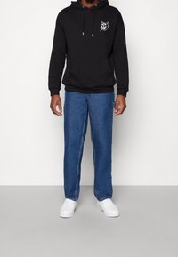 Felpa nera con un design grafico sul petto, abbinata a jeans a gamba dritta blu chiaro e sneaker bianche.