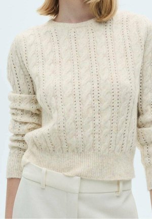 Suéter de punto con cable en color crema con mangas largas remangadas, combinado con pantalones crema de cintura alta sobre un fondo claro.