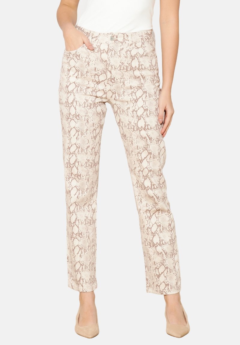 Pantalons en fausse peau de serpent beige avec une coupe slim, poches avant et une texture lisse, stylisés avec un haut blanc ajusté et des chaussures couleur chair.