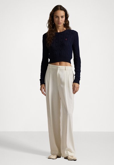 Mornarsko modri pulover s pletenim vzorcem in skrajšano dolžino rokavov, v kombinaciji z visokim pasom, širokimi bež hlačami in kremnimi čevlji.