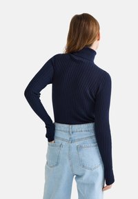 Un haut à manches longues à col roulé côtelé marine associé à un jean en denim bleu clair à taille haute, présentant une coupe légèrement ample et des poches arrière.