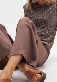 Brun texturerad topp med hög halsringning, kombinerad med ljusbruna vida byxor och bruna sandaler med tjock sula.