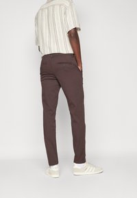 Hnědé kalhoty s úzkým střihem a dvěma zadními kapsami, doplněné krátkým pruhovaným tričkem a bílými teniskami.