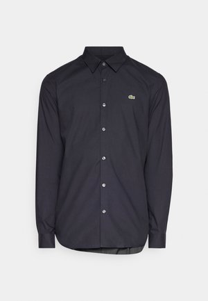 Dark blue long-sleeve shirt featuring a button-down collar, silver buttons, and a green logo on the chest. Made from smooth fabric.