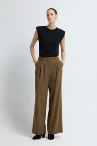 Zwart, nauwsluitend T-shirt met korte mouwen gecombineerd met high-waisted, wijde bruine broek. Laarzen zijn van zwart suède. Lichtgekleurde achtergrond.