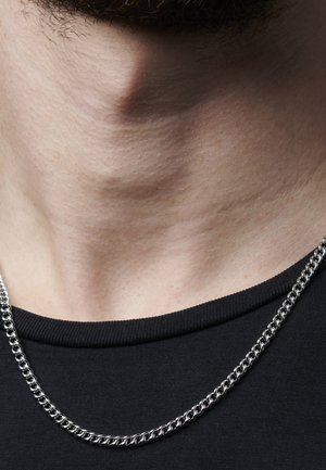 Silver chain necklace with interlocking links, resting on skin above a black shirt neckline, minimal texture visible on skin.