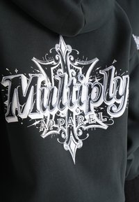 Felpa nera con cappuccio caratterizzata da una grande grafica bianca con caratteri ornamentali che leggono "Multiply Apparel", incorporando elementi decorativi.