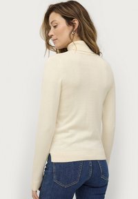 Beige coltrui gemaakt van zachte breiwerkstof, met lange mouwen en een getailleerde pasvorm, met ribbelboorden en een ribbelonderkant.
