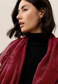 Sheer maroon scarf with a textured floral pattern, draped elegantly over a black turtleneck. Subtle sheen adds visual interest.