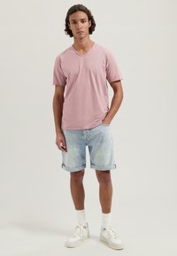 Camiseta de color rosa claro con escote en V, textura suave, combinada con pantalones cortos de mezclilla enrollados en azul claro, usados con zapatillas blancas y calcetines hasta el tobillo.