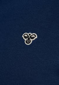 Mała czarno-biała haftowana emblemat pszczoły na środku ciemnoniebieskiego teksturowanego tła tkaniny.