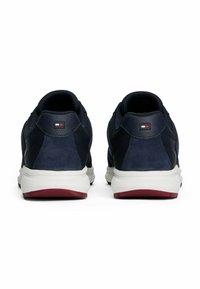 Un par de zapatillas deportivas azul marino con suelas blancas y acentos rojos, vistas desde atrás, con un logo rectangular en el talón.