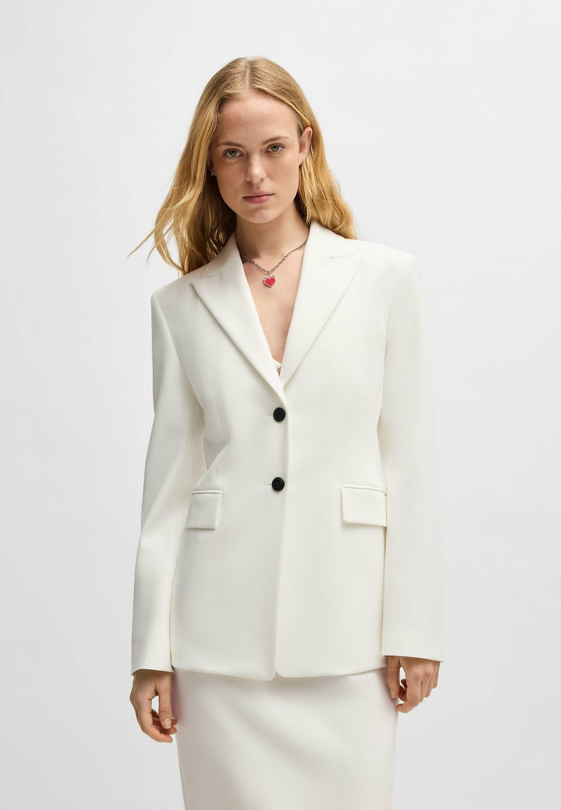 White tailored blazer featuring two buttons, peak lapels, side pockets, and a structured silhouette. Smooth texture with a clean finish.