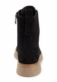 Sort ankelstøvle i ruskind med mellemhøj design og en tekstureret beige sål. Har en lynlås bagpå og synlige stingdetaljer.