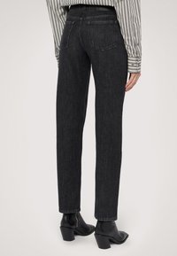 Jeans en denim noir taille haute avec une coupe droite, présentant un design à cinq poches et des détails de couture discrets. Assortis à des bottes noires à talons.